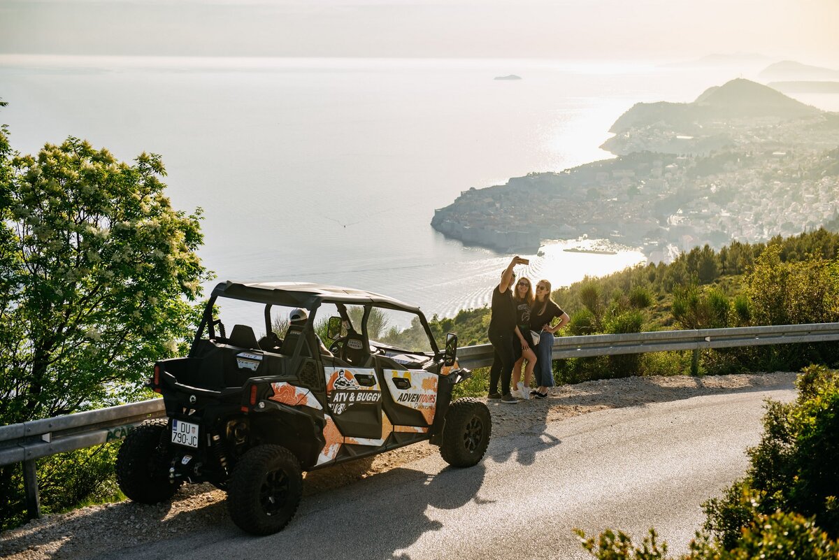 Three persons on a buggy sunset tour taking selfies with the old city of Dubrovnik in the background
